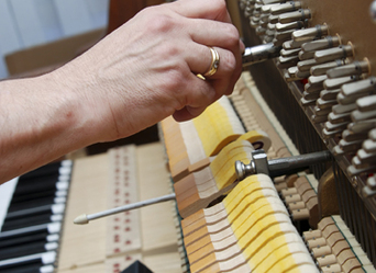Piano technician adjusts the tuning pins on an upright piano.